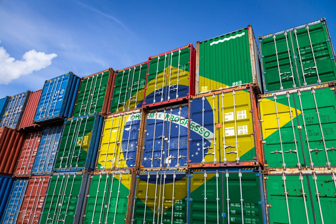 Containers coloridos empilhados com bandeira do Brasil e "Ordem e Progresso" visíveis. Céu azul ao fundo. Atmosfera organizada.
