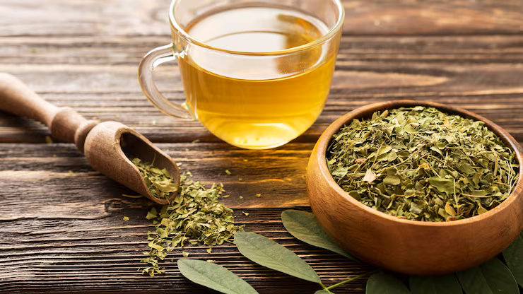 Chá de mate em xícara de vidro ao lado de uma cumbuca com erva-mate seca sobre uma mesa rústica